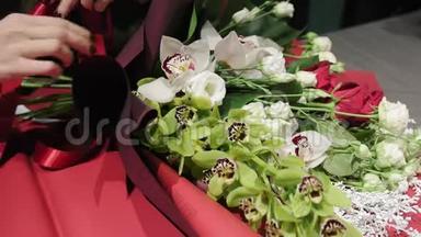 花商把一条丝带系在兰花兰花、红白玫瑰和香果的一束美丽的花束上